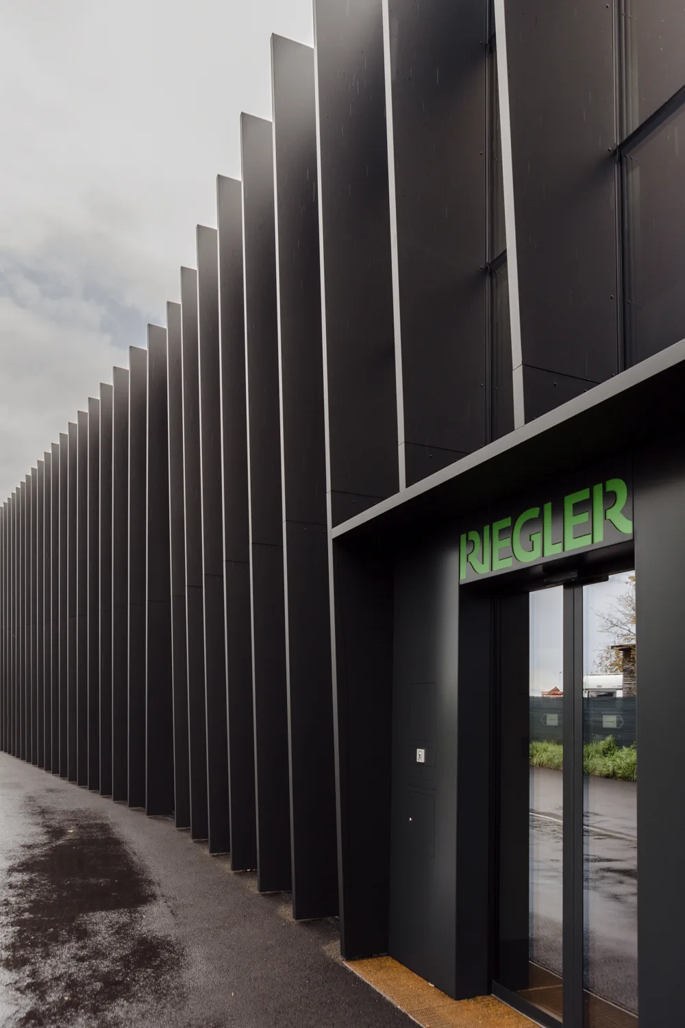 Eingang des Firmengebäudes zwischen schwarzen Lamellen, darüber der grüne Schriftzug RIEGLER