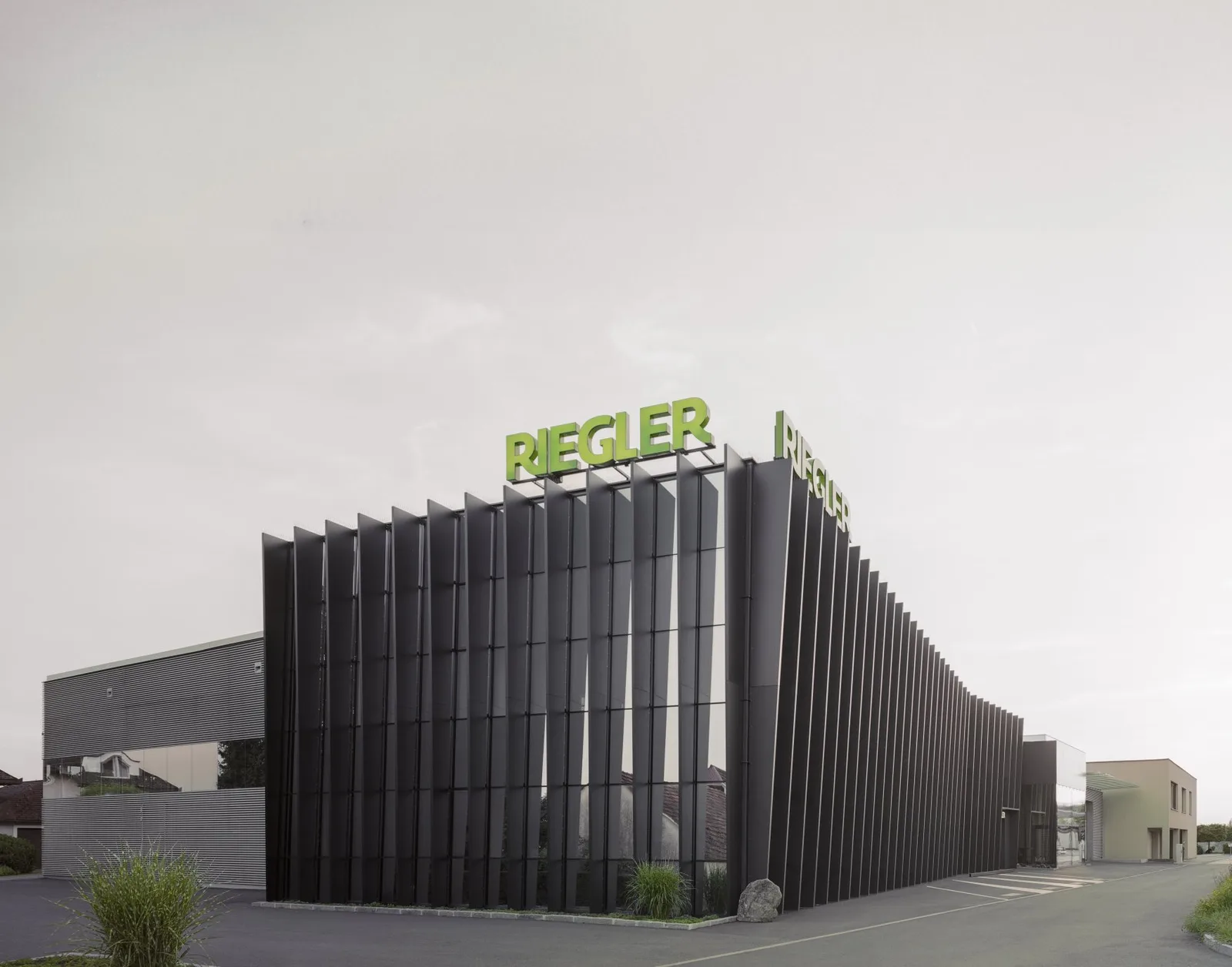Firmengebäude von Riegler Metallbau mit schwarzer Lamellenfassade und grünem RIEGLER-Schriftzug auf dem Dach
