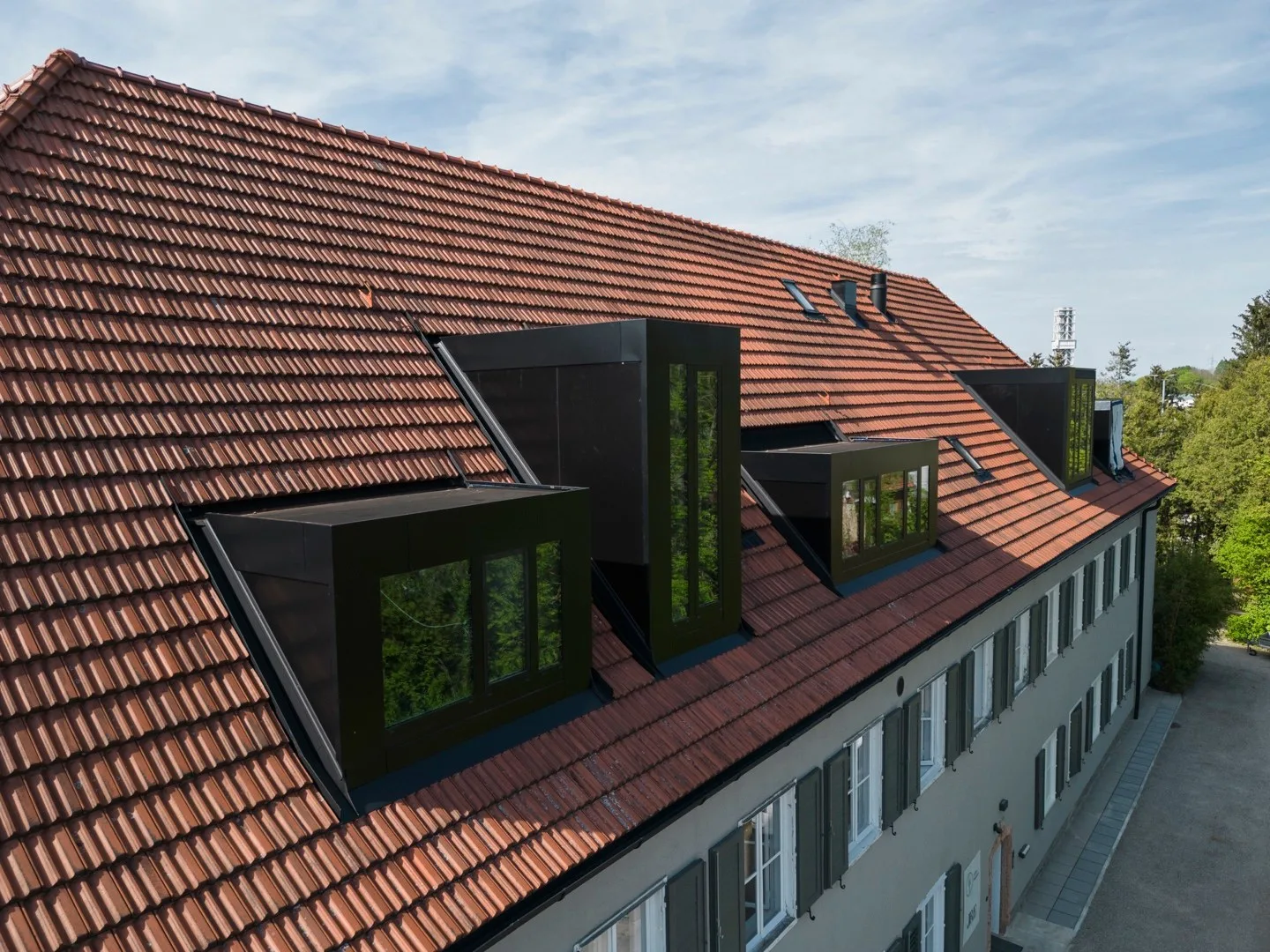 Schwarze Dachgaupen mit großen Glasflächen auf dem roten Ziegeldach eines historischen Gebäudes
