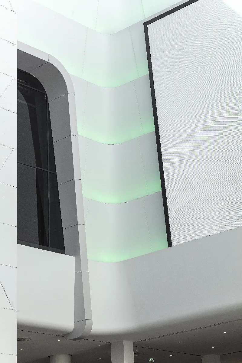 Weiß verkleidete, geschwungene Fassadenteile mit eingelassenen grünen Lichtstreifen