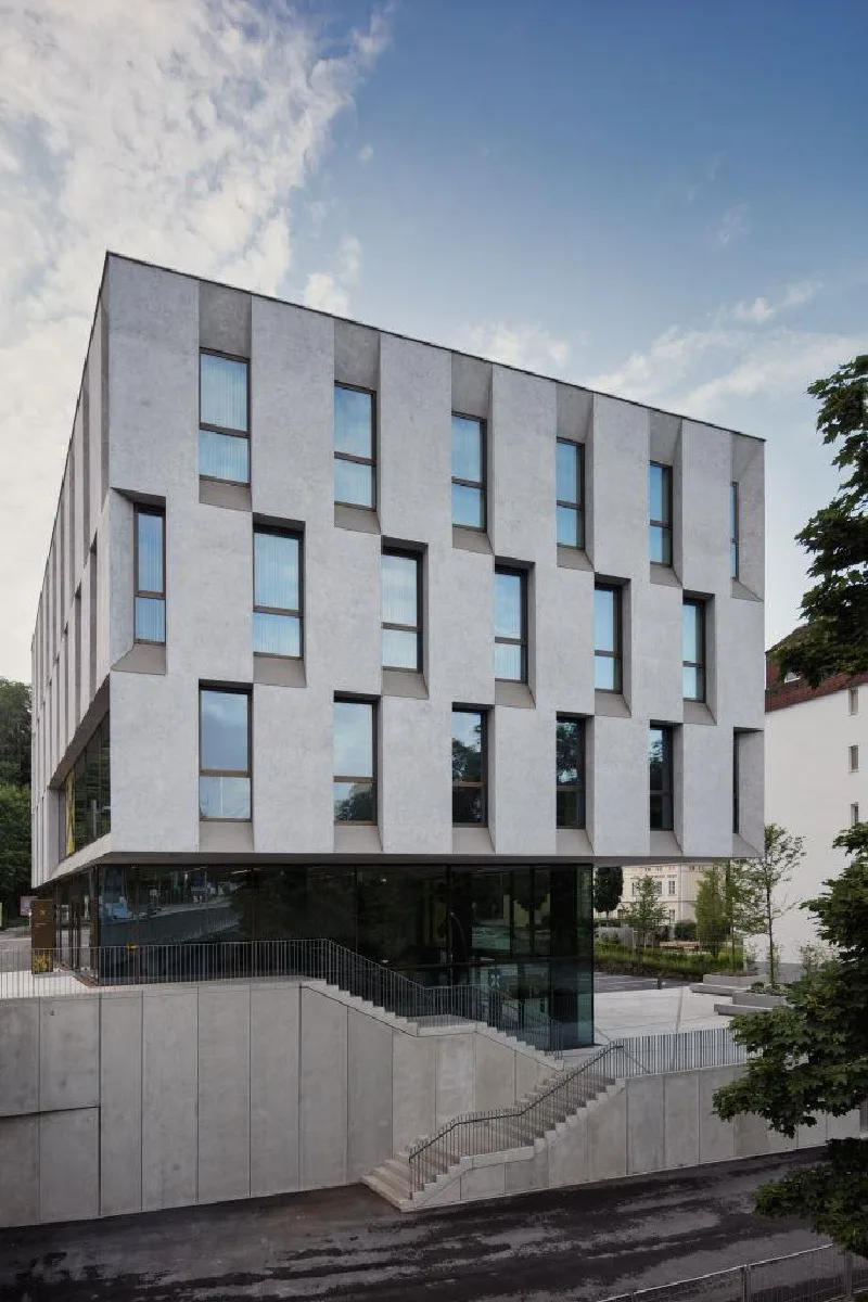 Neubau mit heller Fassade und regelmäßigen Fensterbändern, davor Bäume