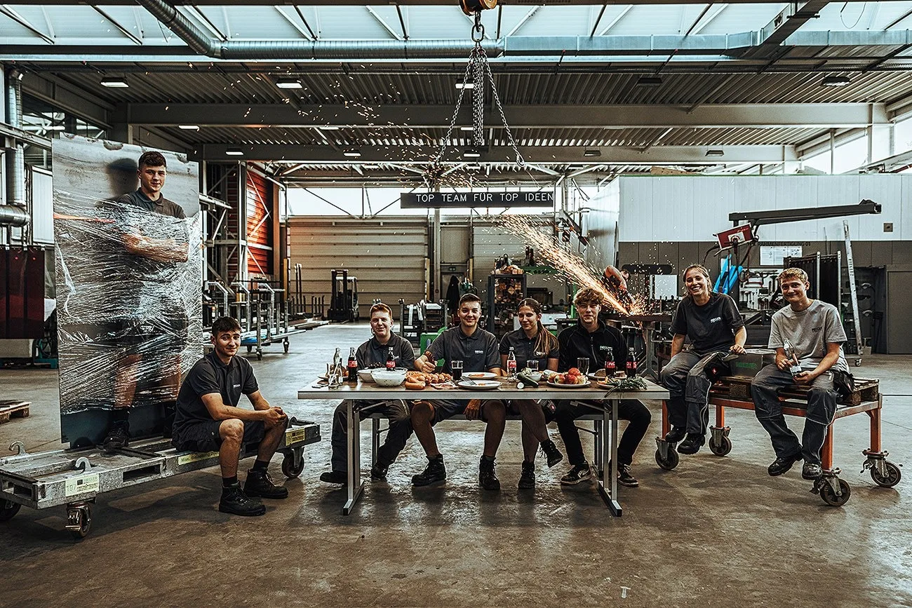 Das Riegler-Team sitzt an einem langen Tisch mitten in der Werkhalle